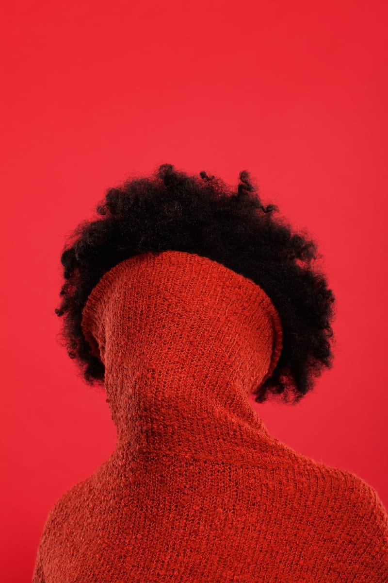 Une femme sur fond rouge avec son col roulé rouge sur le visage. 