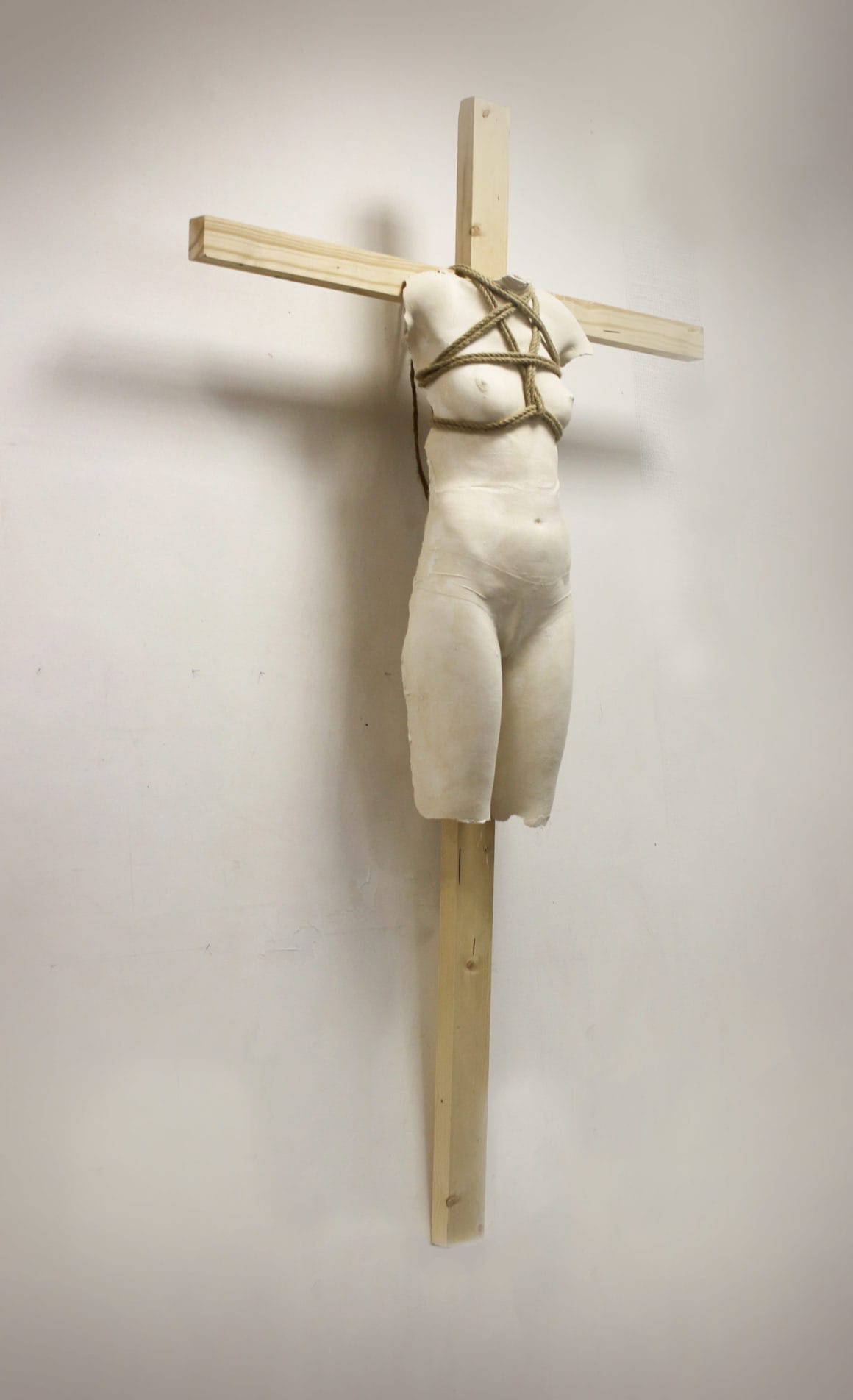 corps de femme en plâtre accroché à une croix avec des cordes de shibari