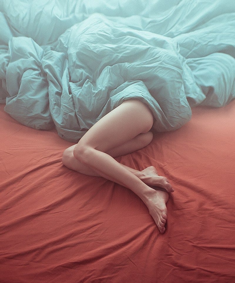 Photographie de Ibai Acevedo, jambes d'une femme qui sortent de sous une couette bleu