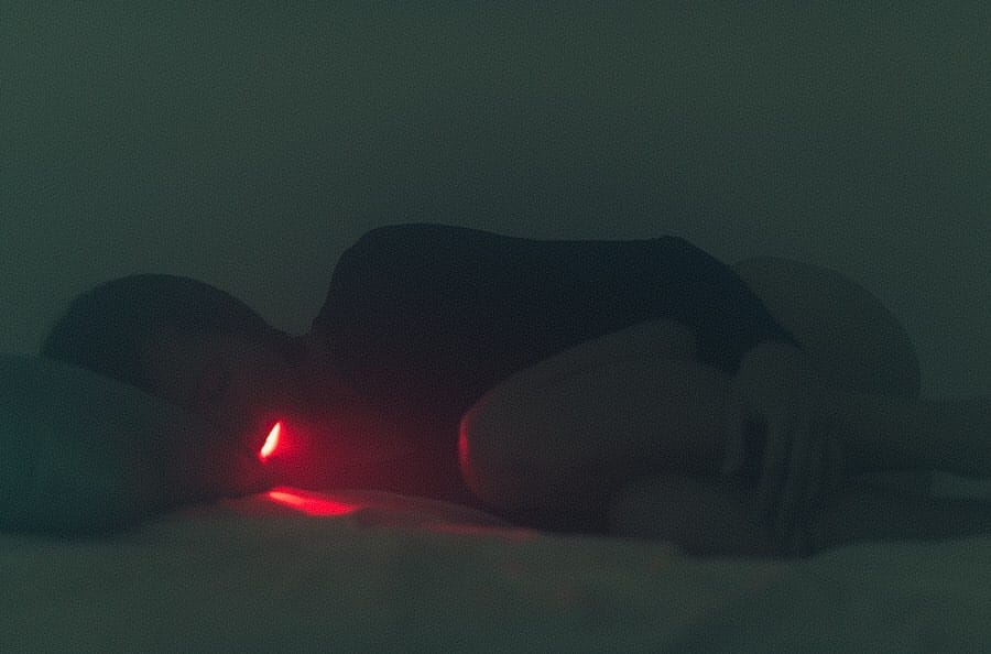 Une femme est allongée recroquevillée sur un lit, une lumière rose semble sortir de sa bouche