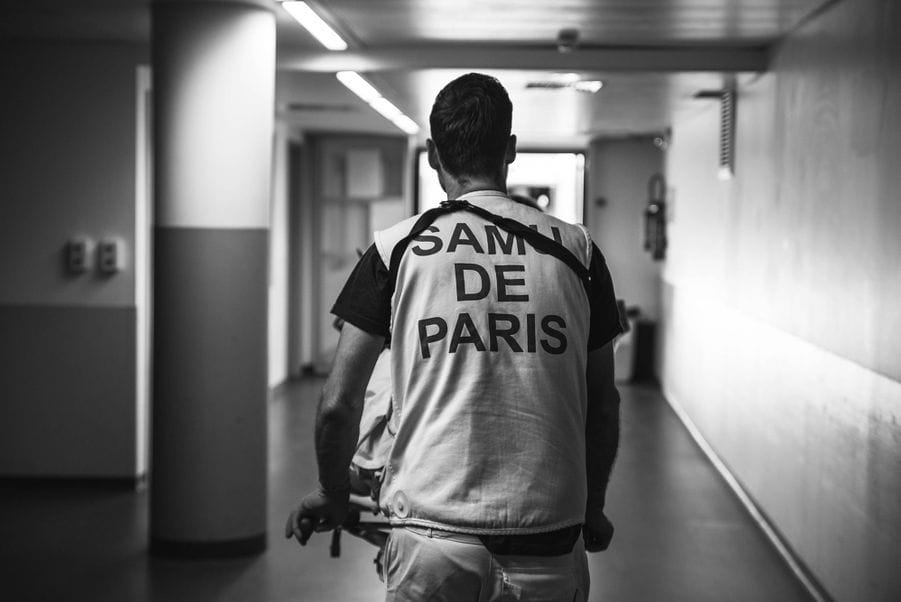 Photo en noir et blanc, homme de dos, sur son vêtement est écrit "SAMU DE PARIS"