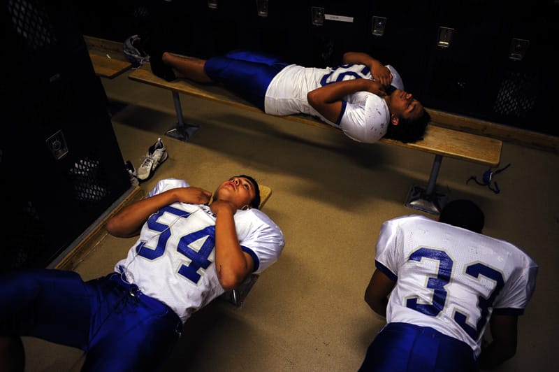 Trois jeunes hommes en tenue de football américain sont allongés sur des bancs de vestiaire et méditent.