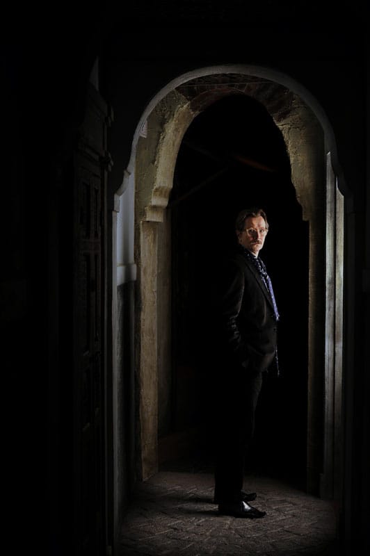 L'actueur Gary Oldman se tient debout, dans un couloir sombre en pierre.