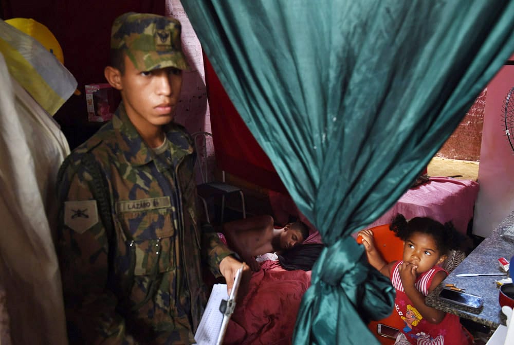 Un militaire inspecte un logement de fortune, devant une petite fille curieuse. EN arrière plan, un jeune homme dort.