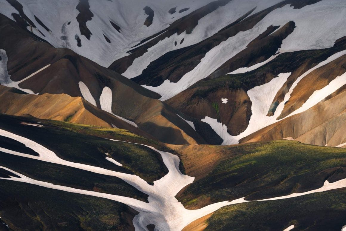 Plan de vallons bruns et verts, avec de la neige blanche. Les volumes forment une image presque abstraite.
