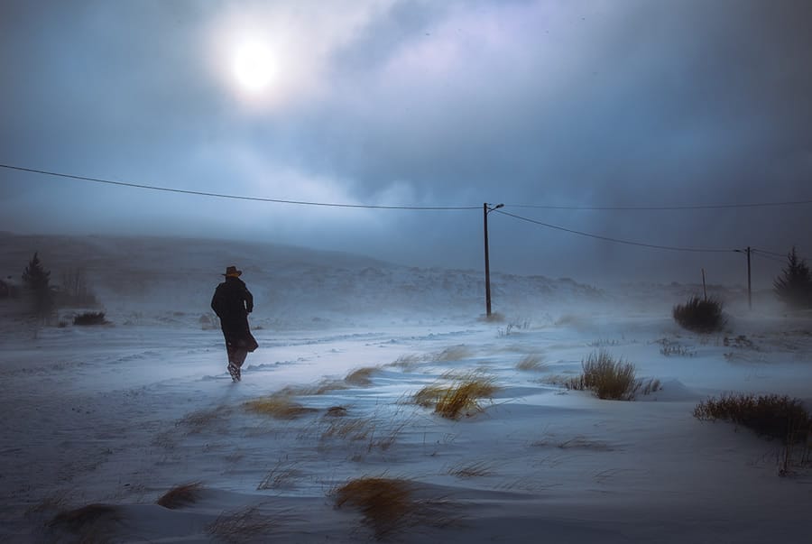 Cette photo montre un homme avec un chapeau de dos marchant dans la neige