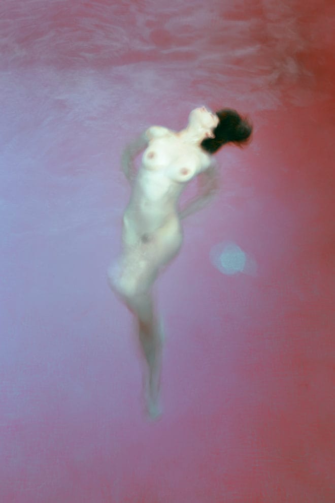 Photographie d'une femme nue dans une étendue d'eau rose.