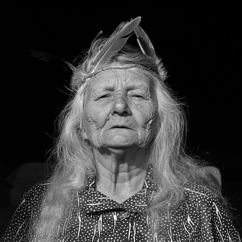 Photographie d'une vieille femme avec des plumes sur la tête.
