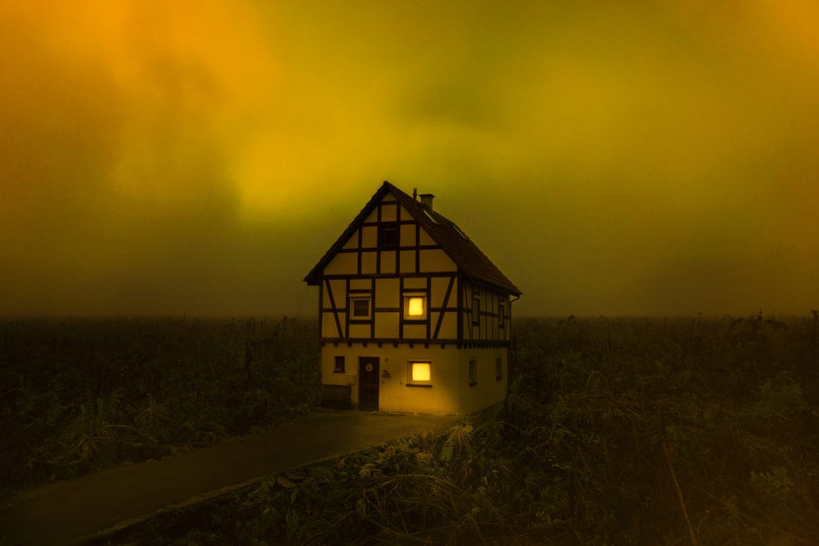 Photographie d'une maison au milieu d'un champs avec un ciel jaune et vert.