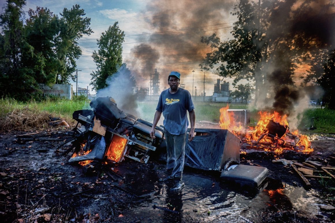 Giles Clarke photographie un homme devant des carcasses de voitures en feu 