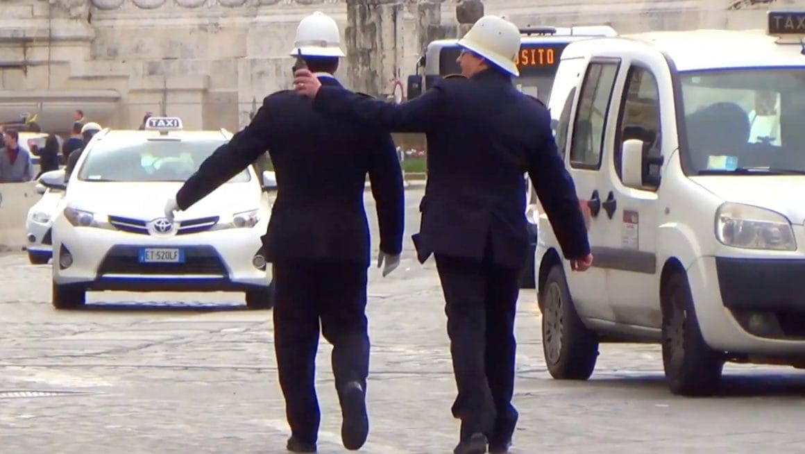 Deux policiers britanniques saluant des passants, en traversant une route urbaine.