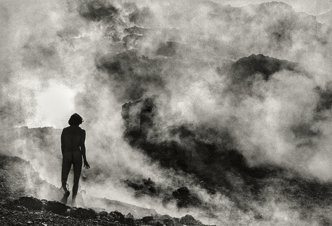 dans un nuage de fumée se dessine en noir et blanc une silhouette qui marche sur des rochers