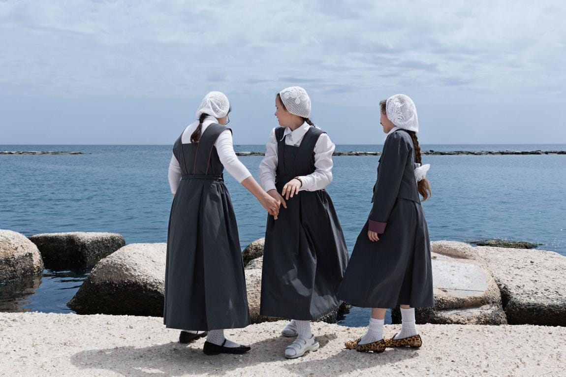 trois jeunes filles avec des habits du dimanche se tienne sur une digue, au loin la mer est calme