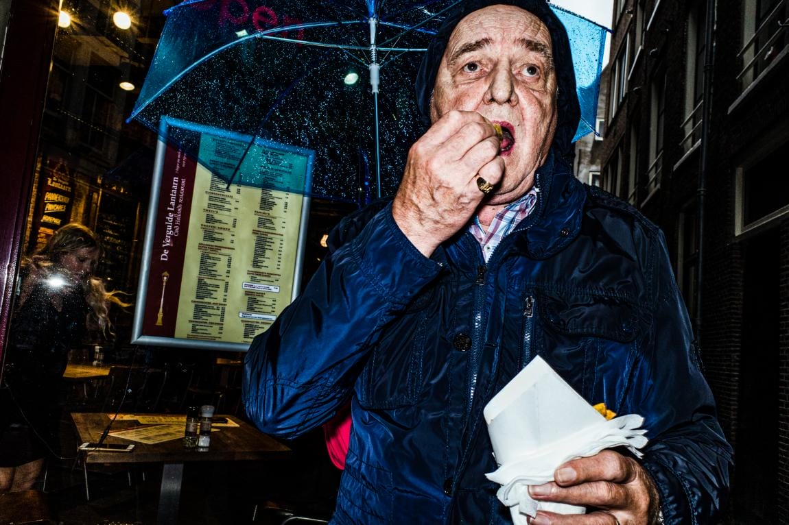 pris sur le vif, un papi mange des frites dans la rue, abrité par un parapluie