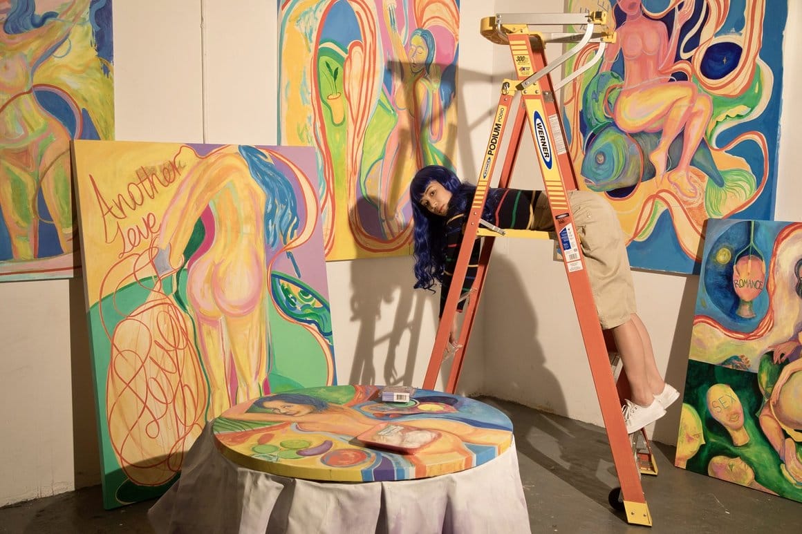 L'artiste Lily Fei dans son atelier sur une échelle, entourée de peinture