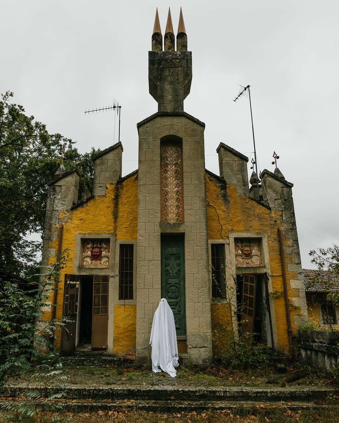 devant la porte d'une chapelle jaune armée d'antennes, le fantôme regarde pensivement ailleurs