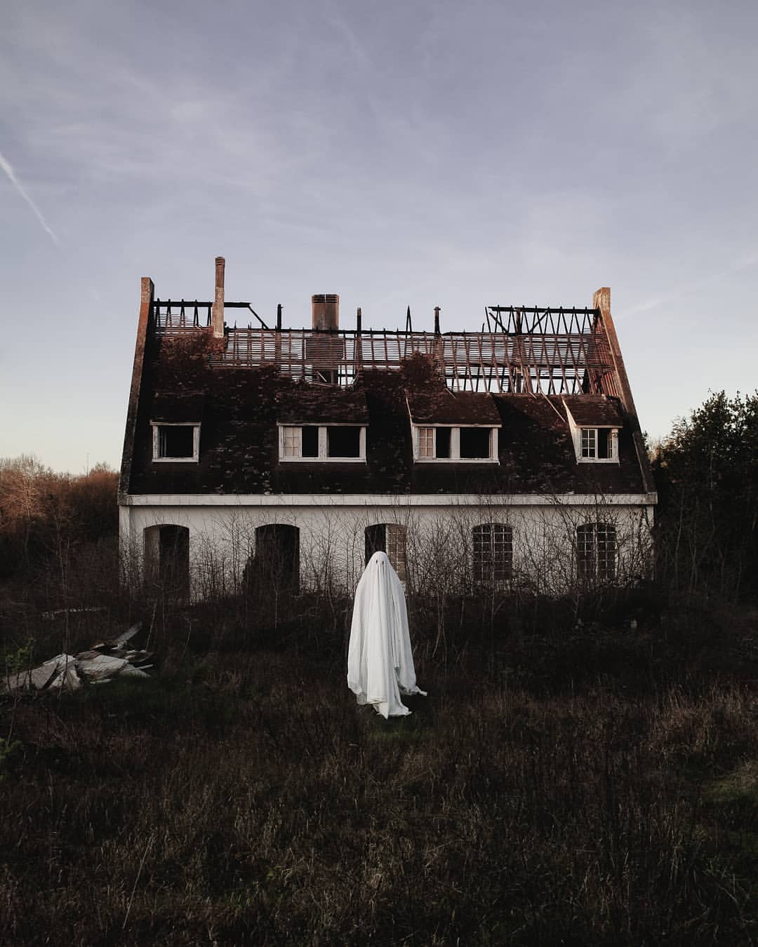 au lever du jour, devant une maison dont le toit est complètement détruit ou pas terminé, le fantôme nous regarde.