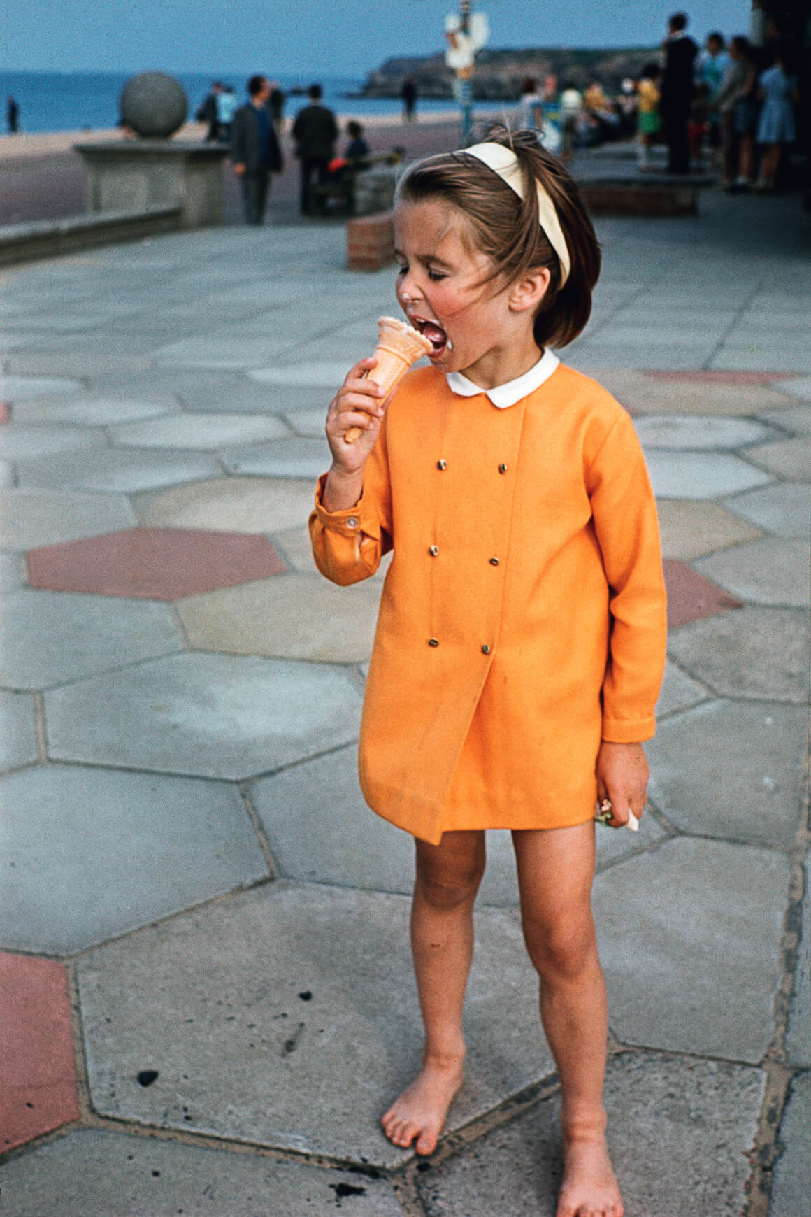 lee shulman anonymous project, petite fille au manteau orange qui déguste une glace en bord de mer