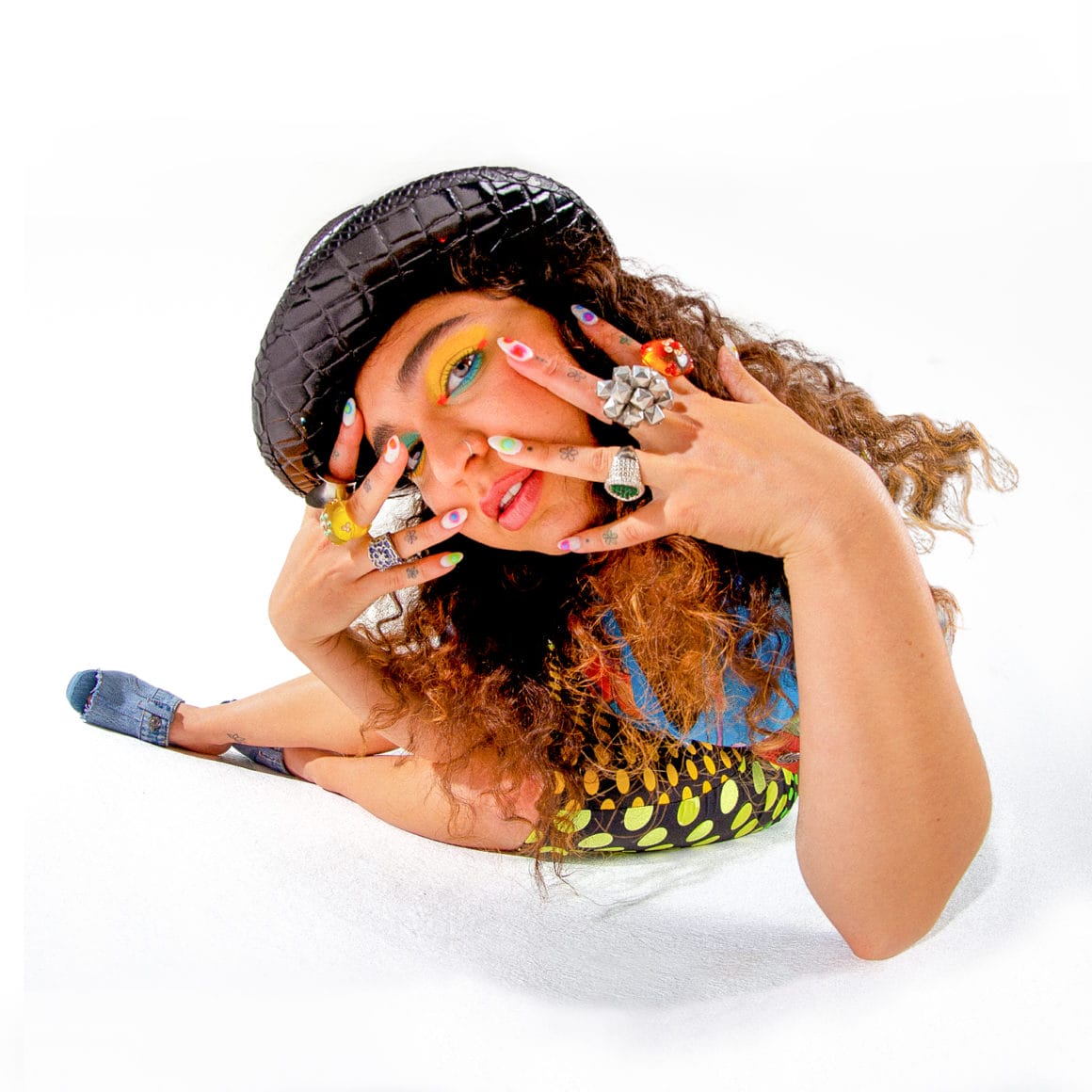 photographie de la chanteuse pop en effet fisheye, elle porte un chapeau ciré, de grosses bagues, un maquillage coloré et des ongles vernis