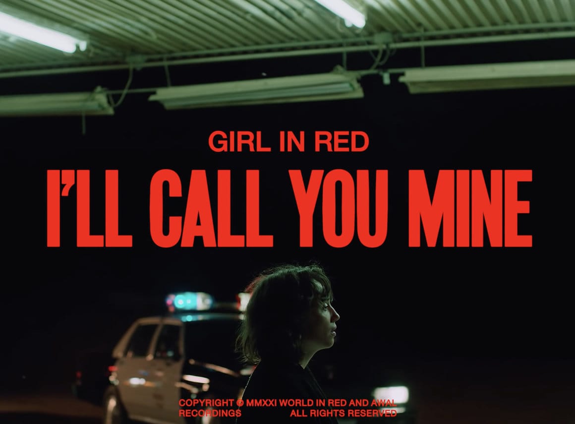 Scène d'introduction du clip "I'll Call You Mine". En bas du cadre, un des personnages se tient de profil. Derrière elle, des voitures de police arrivent. En rouge, au centre de l'écran, est affiché  le titre du clip.