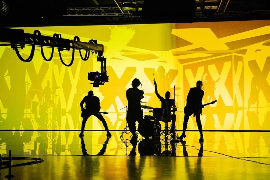 Photo du groupe The Rasmus sur le set du clip de "Jezebel". Silhouettes sombre sur fond jaune.