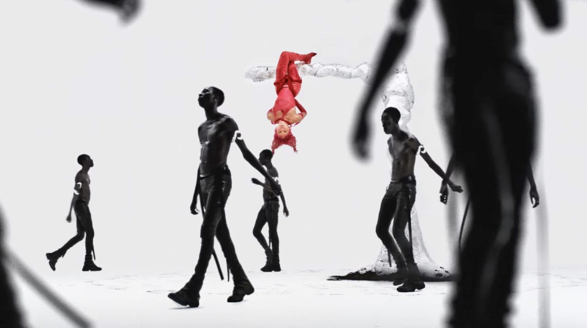 Capture d'écran du clip "Other Men". Crystal Murray se tient, tête en bas, toute vêtue de rouge, sur la branche d'un arbre argenté. Un homme peint de noir et divisé en plusieurs silhouettes, fait les mille pas, au sol.