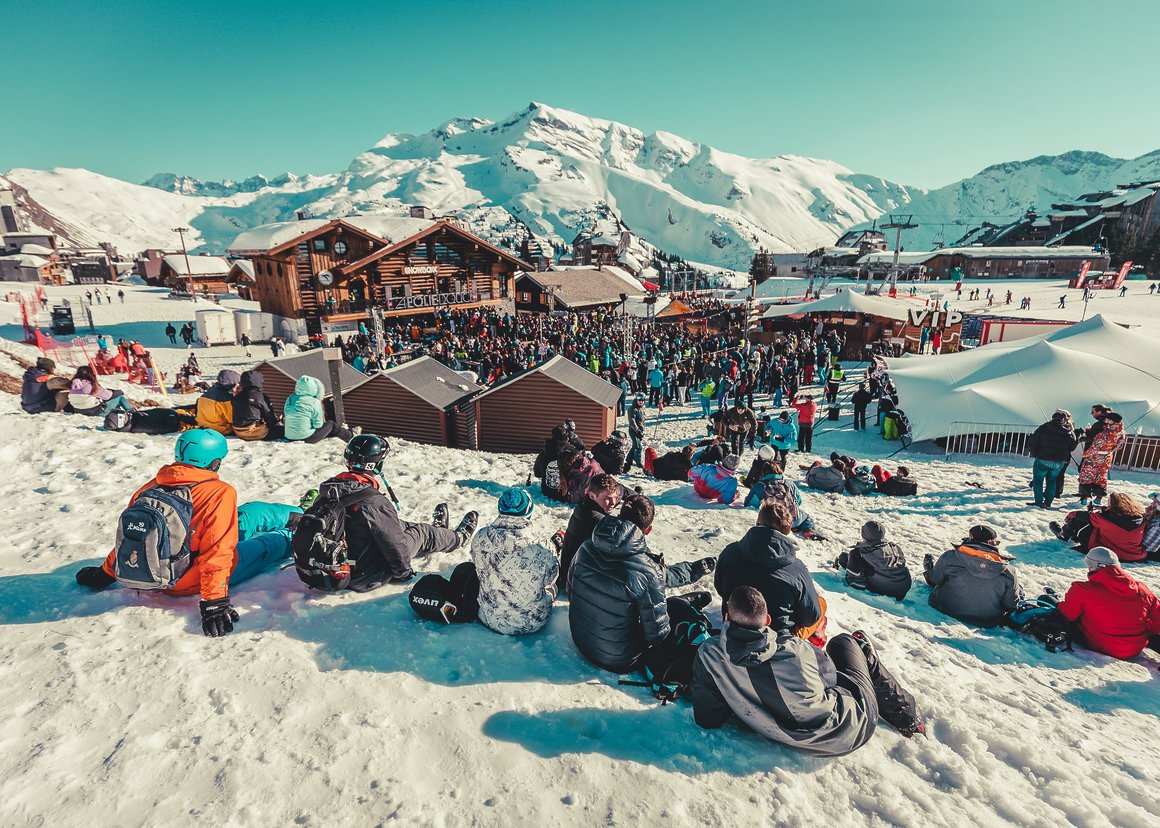 Photo du festival Snowboxx. On y voit des châlets, des gens sur des pistes de ski et des montagnes en fond.