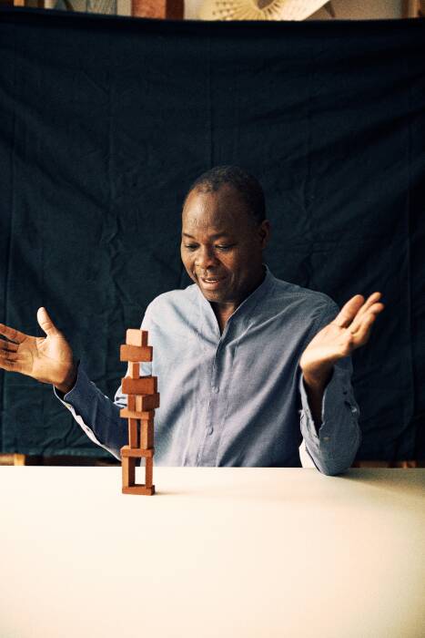 Photo de Diébédo Francis Kéré avec une tour en bois face à lui