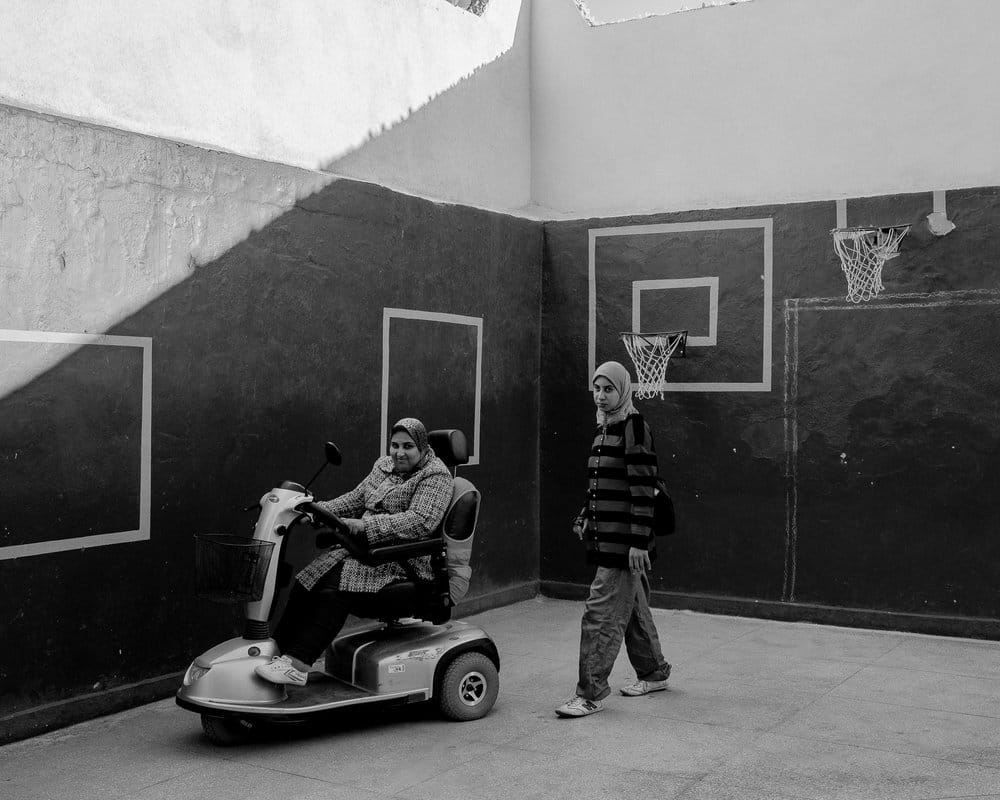 Une femme marocaine est sur une chaise roulante électrique sur un terrain de basket accompagnée d'une jeune femme. 