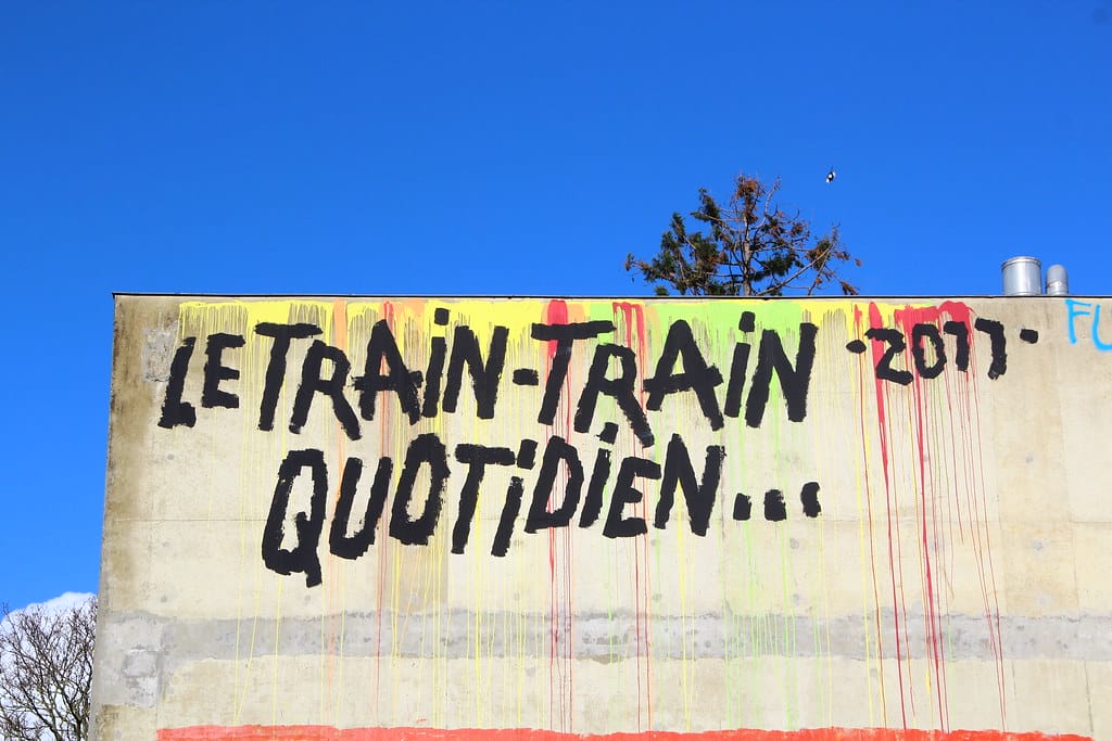 "le train-train quotidien" inscrit en graffiti le long de la voie ferrée