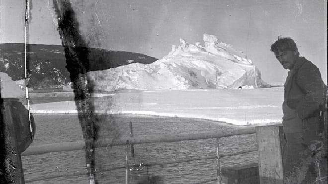 Cette photo a été prise sur le bateau d'exploration, l'un des membres de l'équipage se tient debout et un ilot de glace apparaît derrière lui.