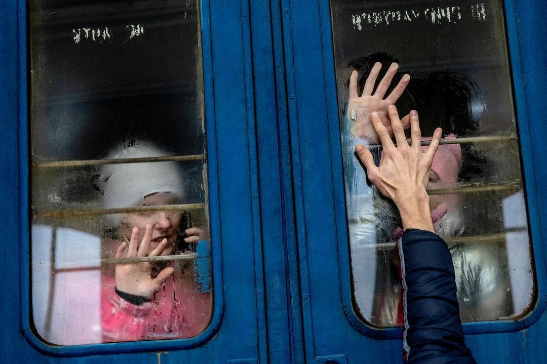 Deux petites filles sont dans un wagon bleu. La main de leur proche, un soldat ukrainien, pose sa main sur la vitre pour dire au revoir à sa famille