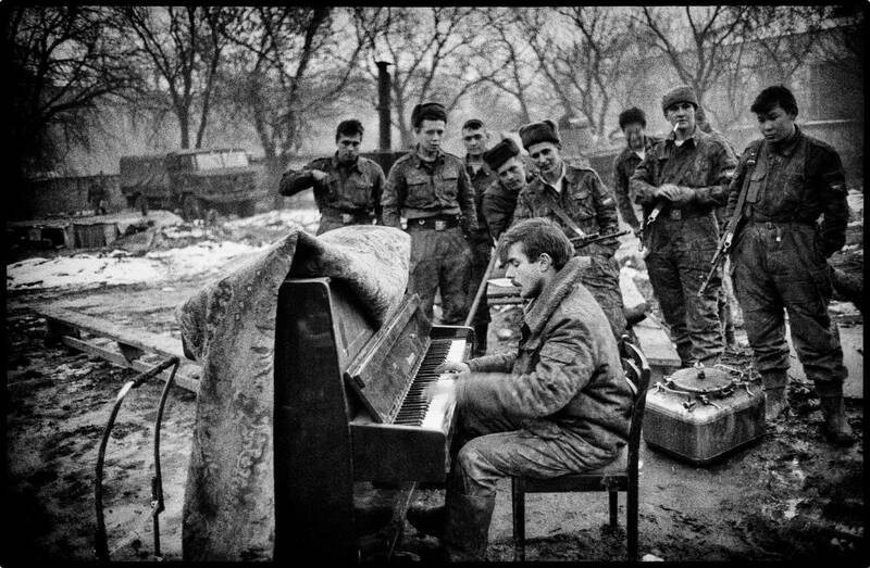 Photo en noir et blanc d'un soldat jouant du piano pour ses collègues dans un paysage chaotic.