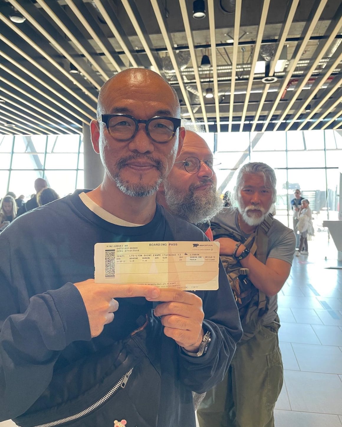 Photo de Kim Jung Gi dans un aéroport heureux de montrer à la caméra son billet partant de Lyon en direction de Lisbonne 