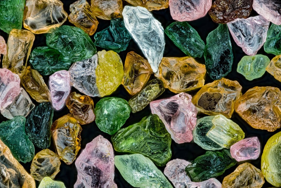Photo of Alaskan sand seen under a microscope.  It represents dozens of green, yellow, orange and pale pink crystals.