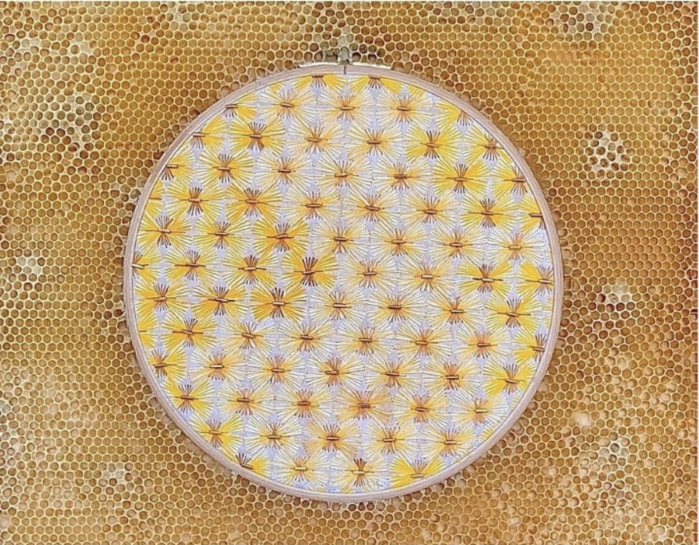 Broderie représentant un motif blanc, jaune et cuivré avec des perles, disposée dans une ruche