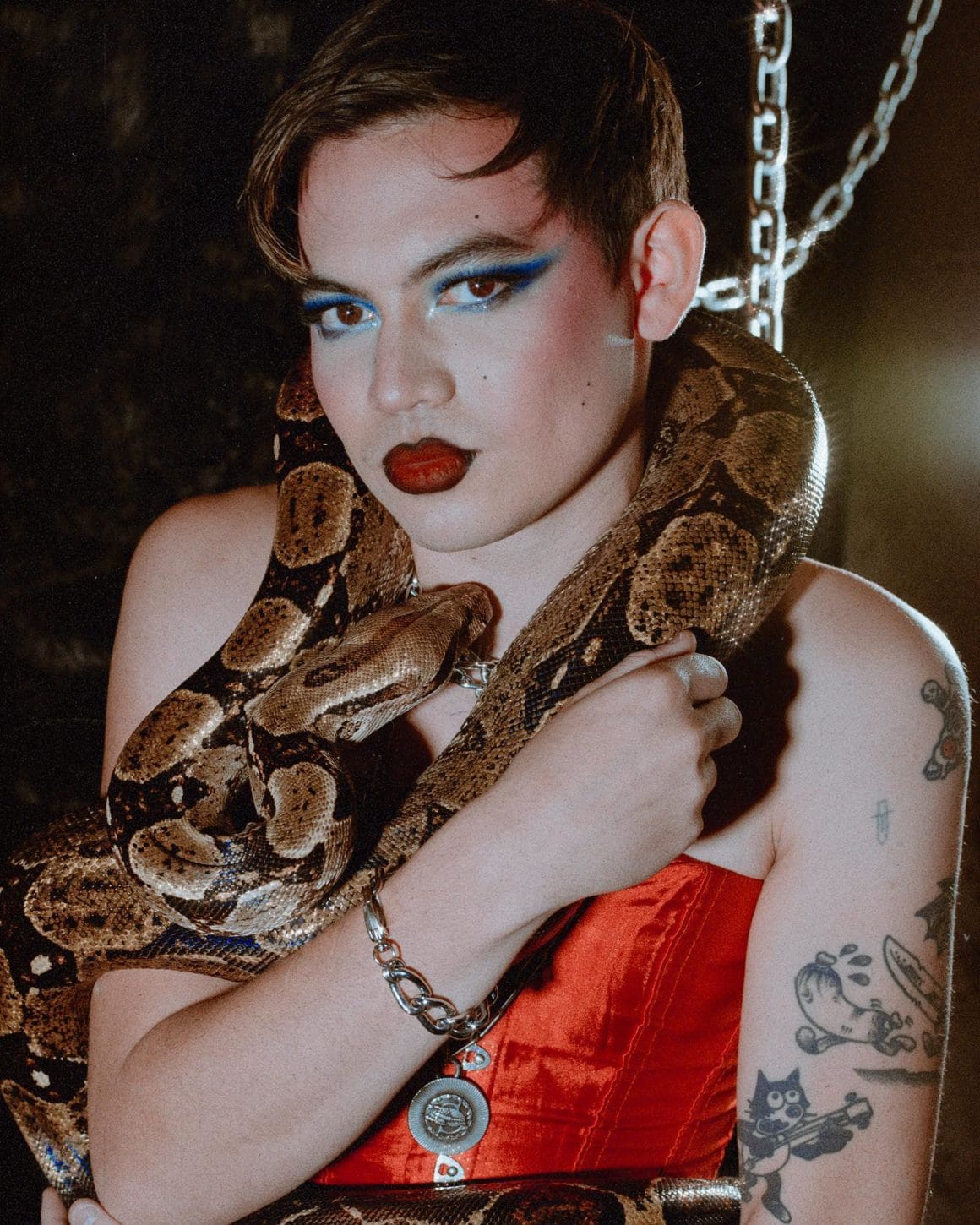 L'artiste Jimmy Knives pose maquillé et habillé d'un corset rouge avec un serpent autour du cou