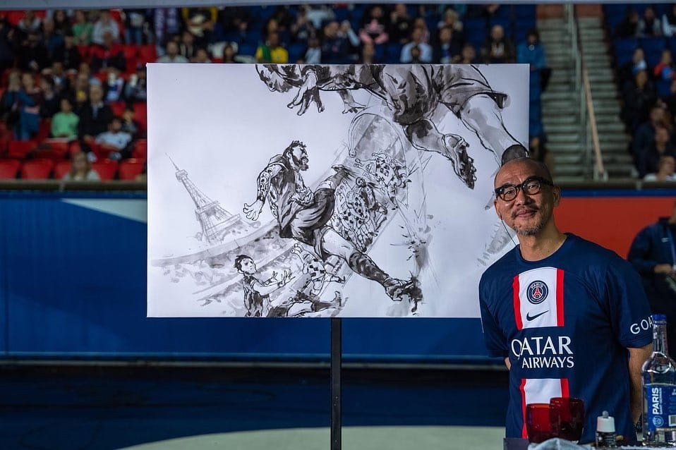 L'artiste Kim Jung Gi pose devant son oeuvre représentant un match de foot français dans le stade des princes à paris. Il est vêtu d'un t-shirt du PSG
