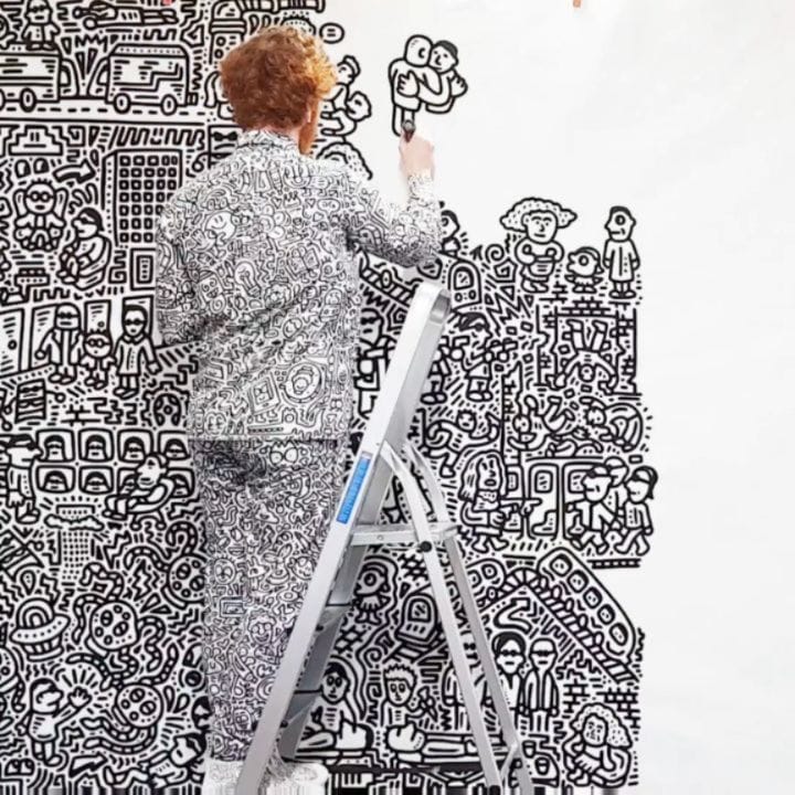 L'artiste Mr. Doodle est sur un échafaudage, en pleine performance de sa fresque noir et blanche.