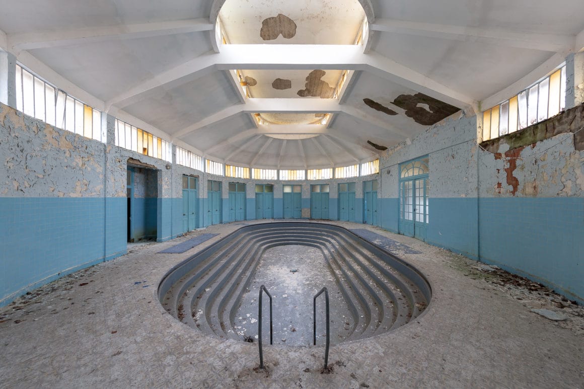photo d'une piscine vide et abandonnée en intérieur, les murs sont délabrés